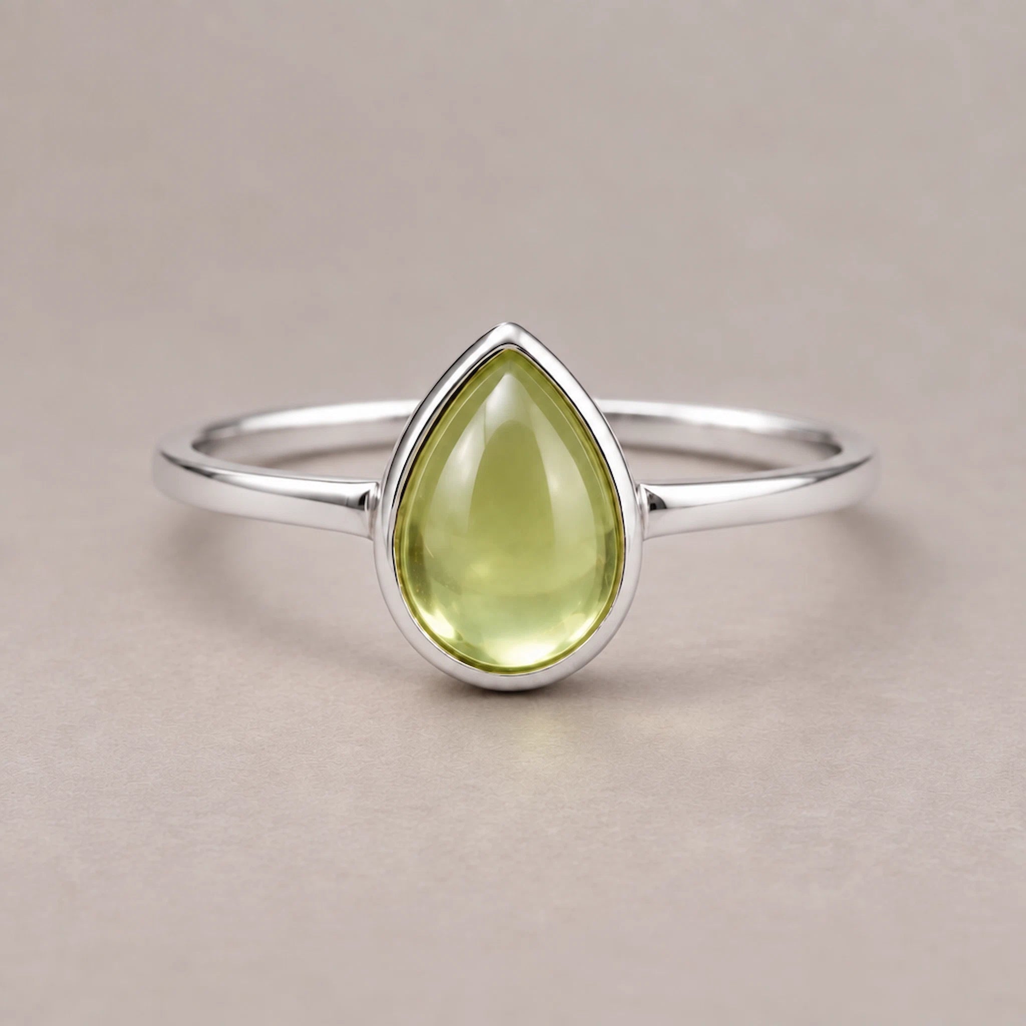 Silver august birthstone ring with a green teardrop-shaped natural peridot gemstone on a beige background