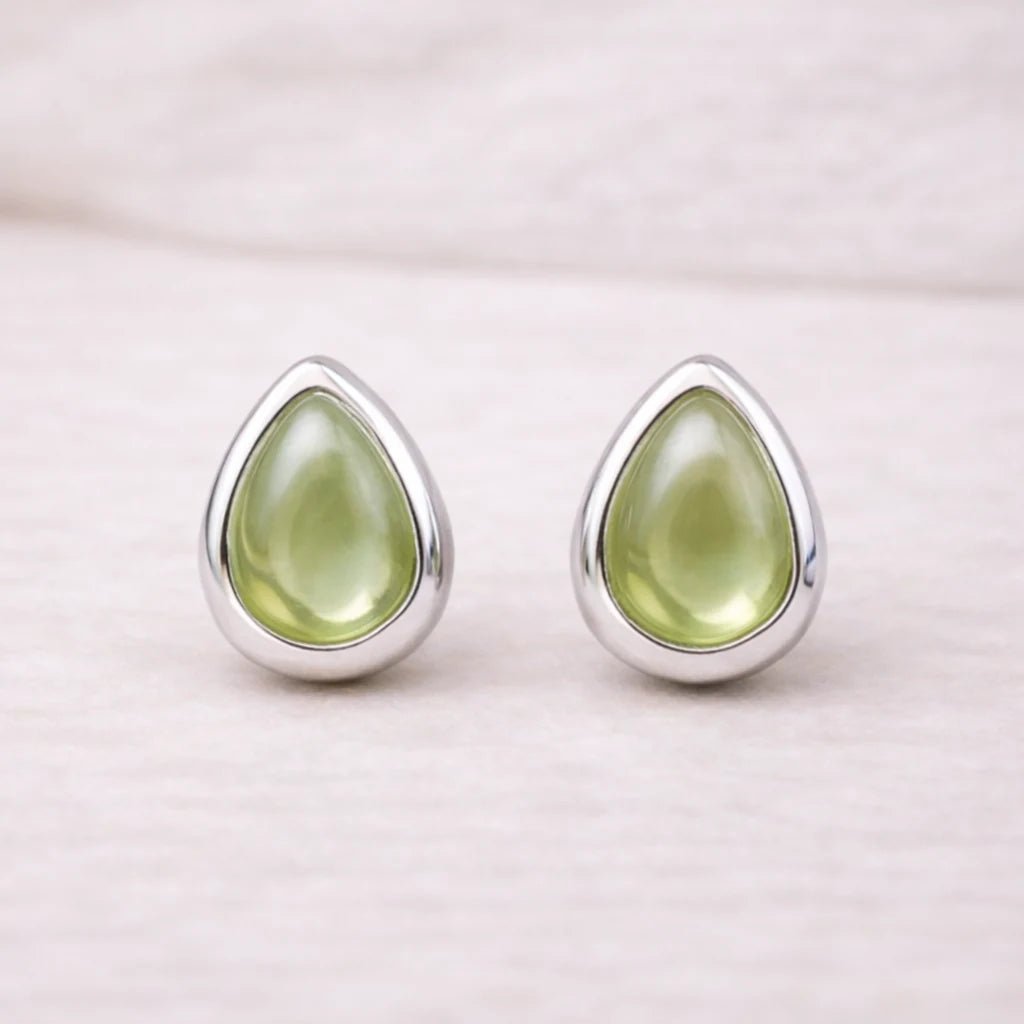 Teardrop-shaped green natural peridot gemstone earrings with sterling silver settings on a light pink background