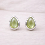 Teardrop-shaped green natural peridot gemstone earrings with sterling silver settings on a light pink background