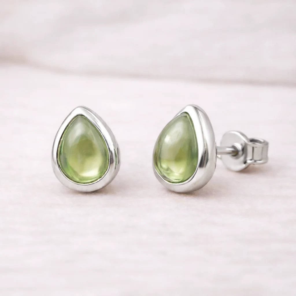 Teardrop-shaped green natural peridot gemstone earrings with sterling silver settings on a light pink background