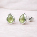 Teardrop-shaped green natural peridot gemstone earrings with sterling silver settings on a light pink background