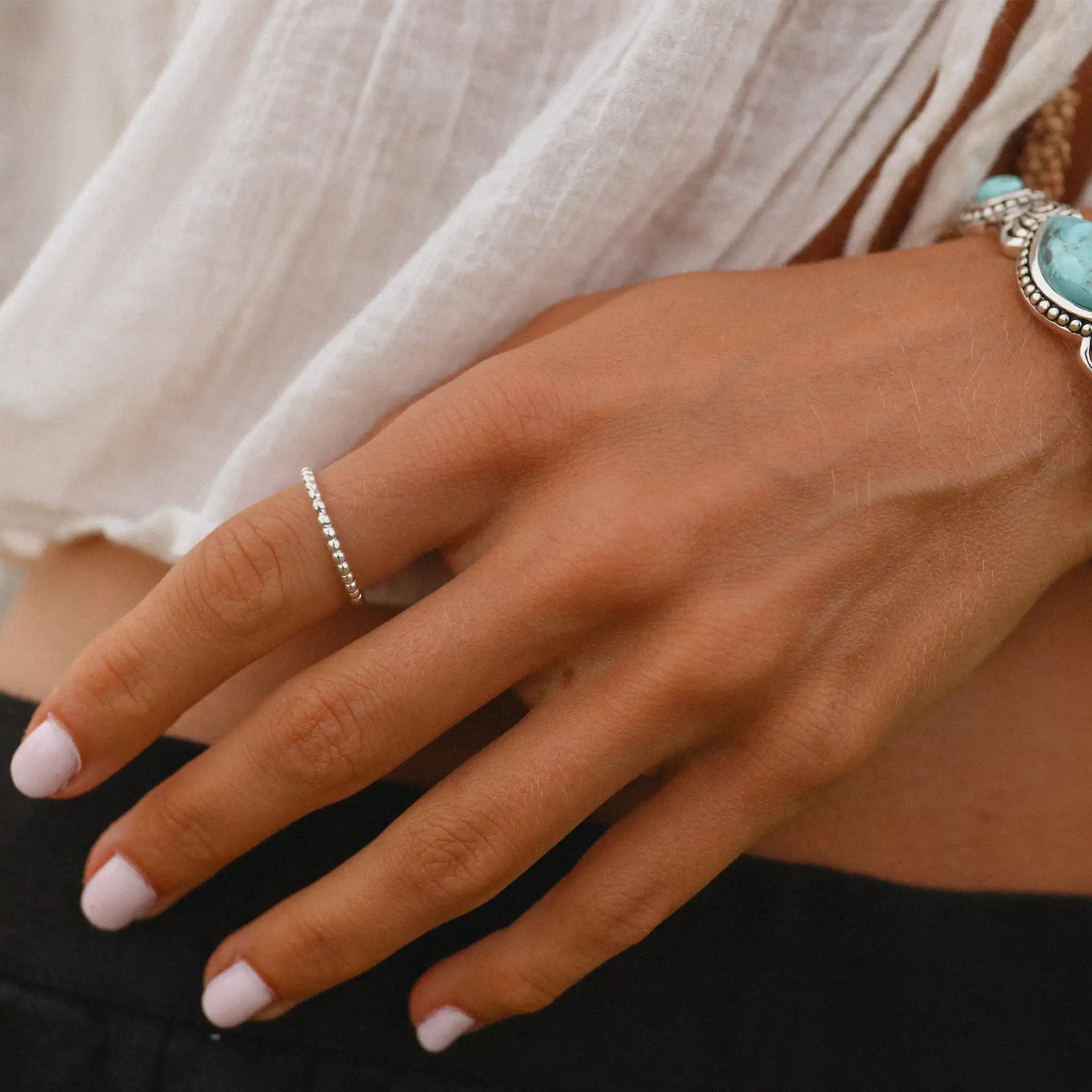 Close-up of a hand wearing a sterling silver stacker ring with a blurred background
