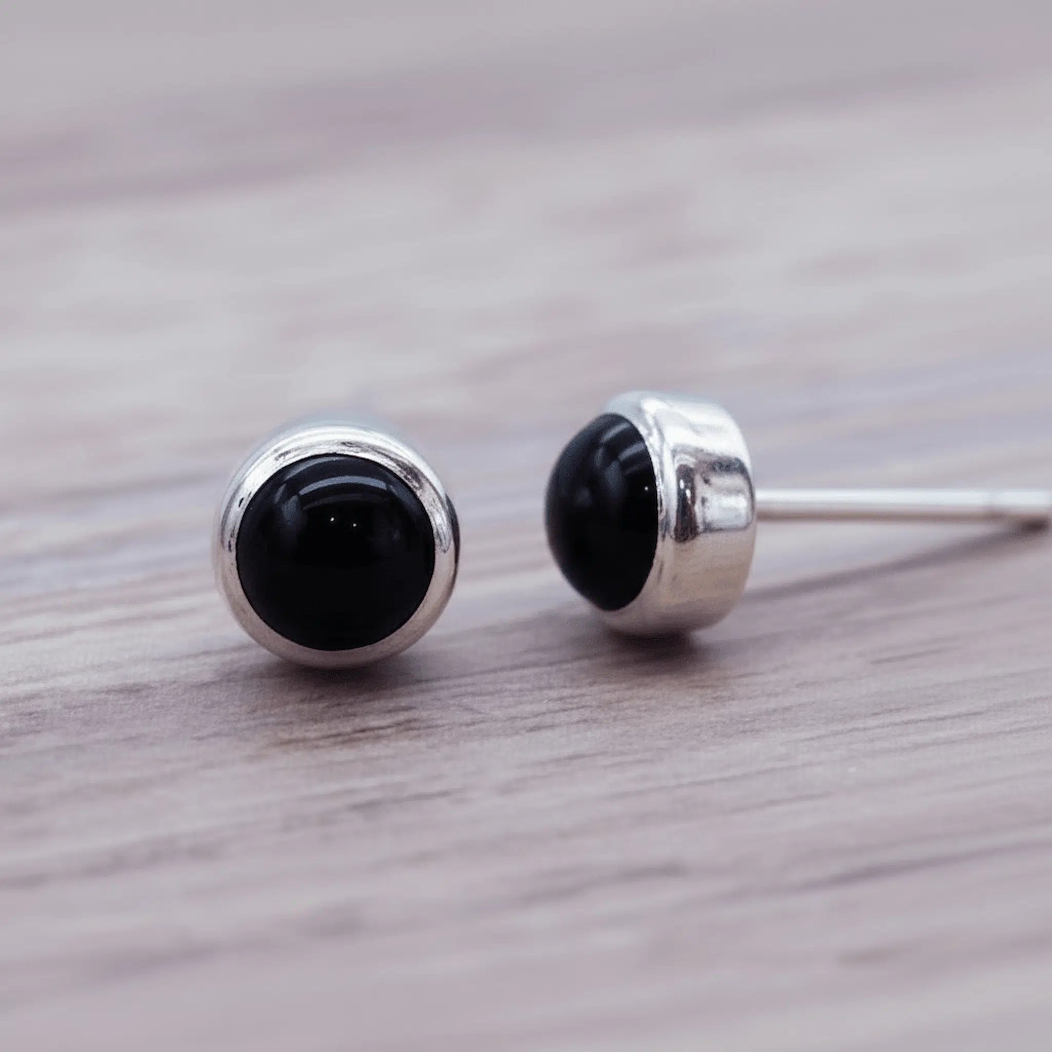 Pair of natural black onyx gemstone stud earrings with silver posts on a wooden surface