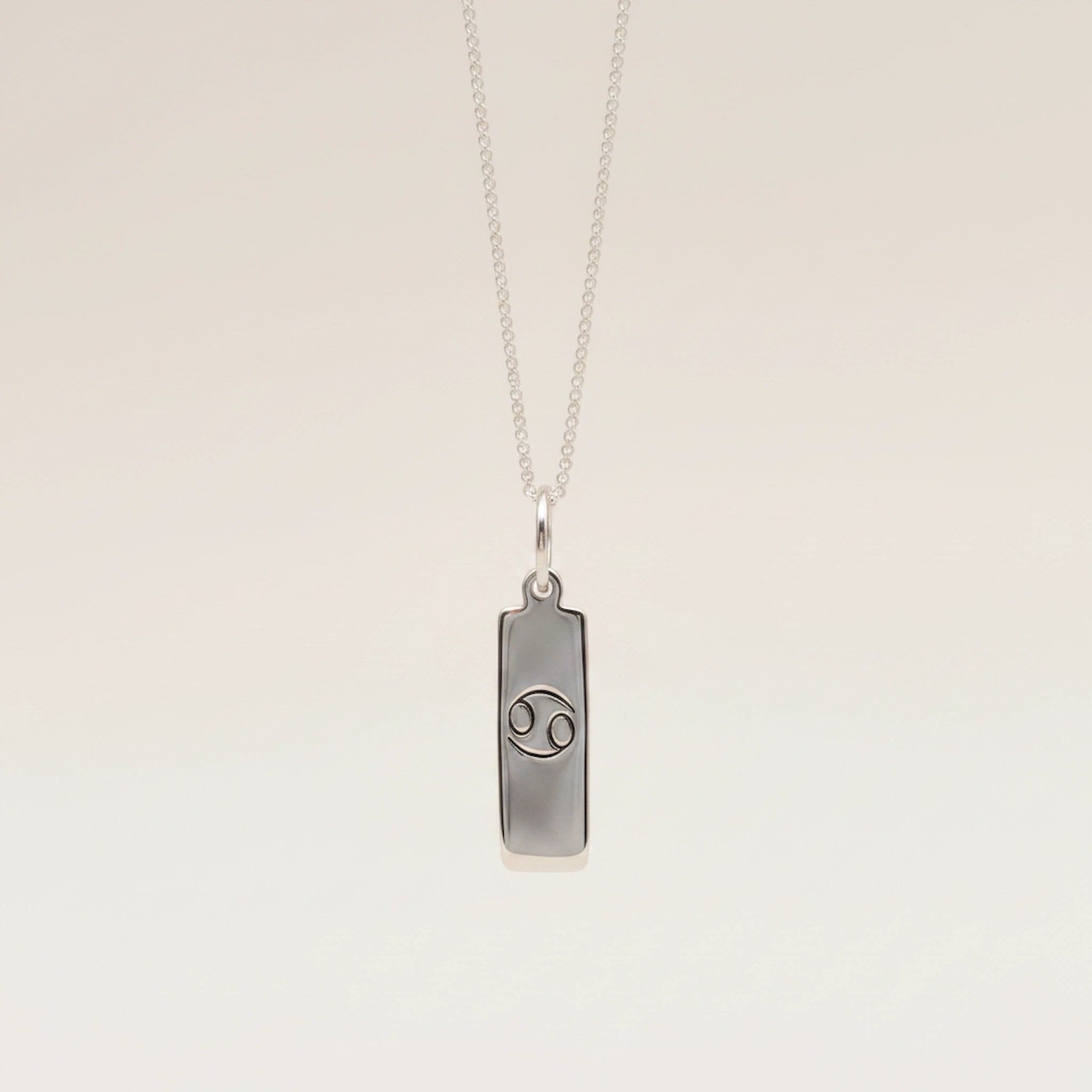 Silver necklace with a cancer zodiac pendant on a beige background