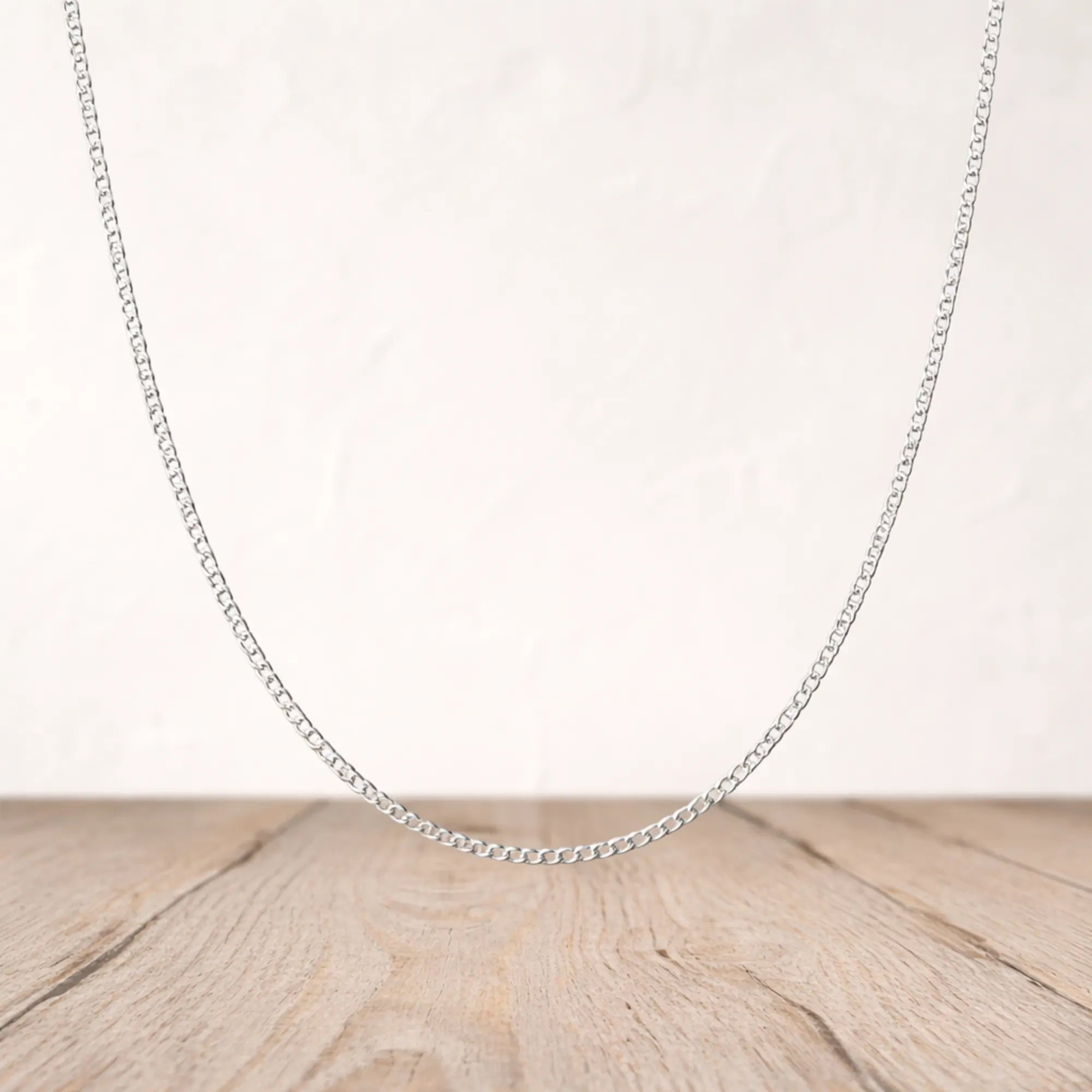 Silver chain necklace on a wooden surface with a light background