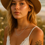 Woman wearing a straw hat, sterling silver chain necklace and white top with a blurred natural background