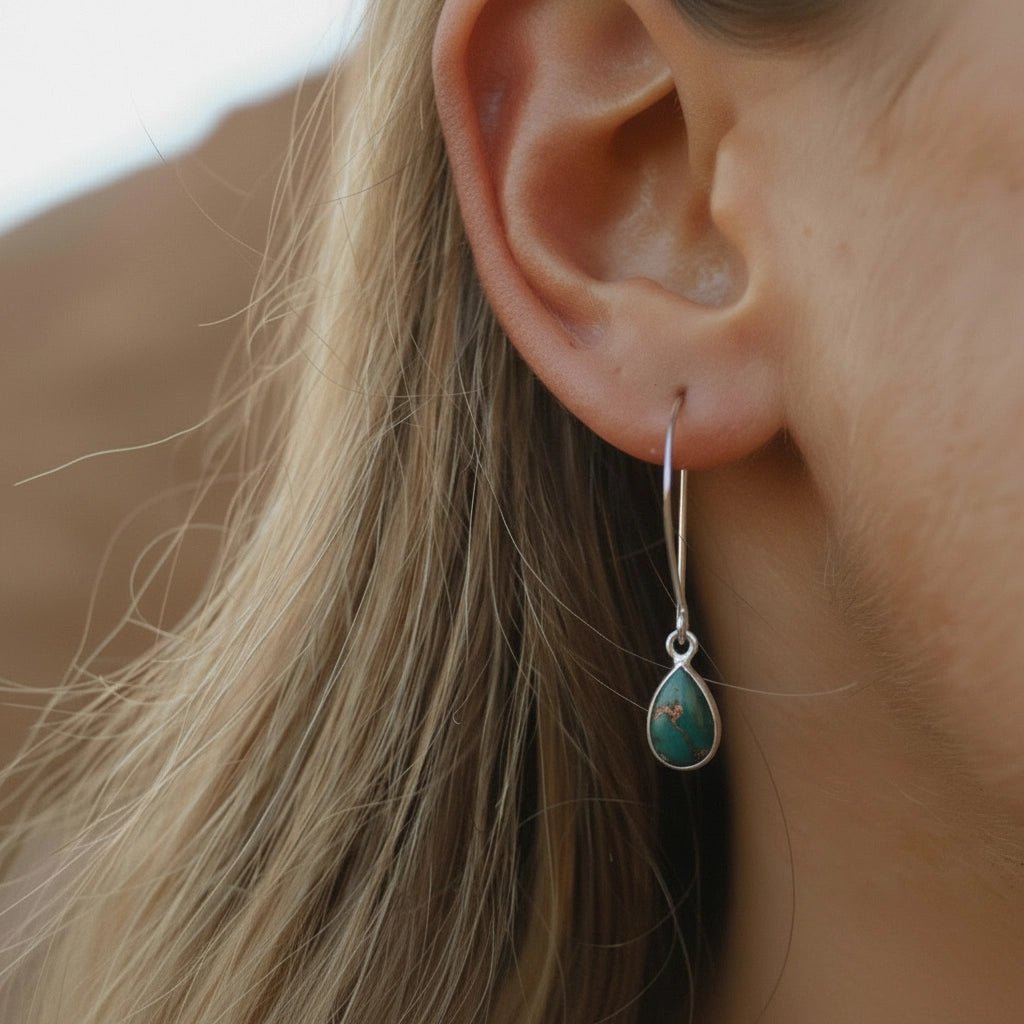 Close-up of an ear wearing a turquoise teardrop earring with blurred background