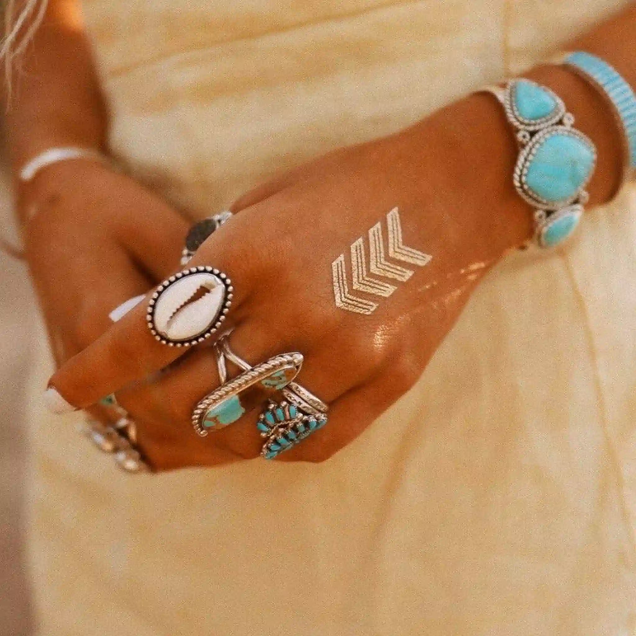 Close-up of a hand wearing multiple bracelets with turquoise stones on a beige background