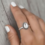 Silver ring with a central cowrie shell stone on a person's finger against a wooden background