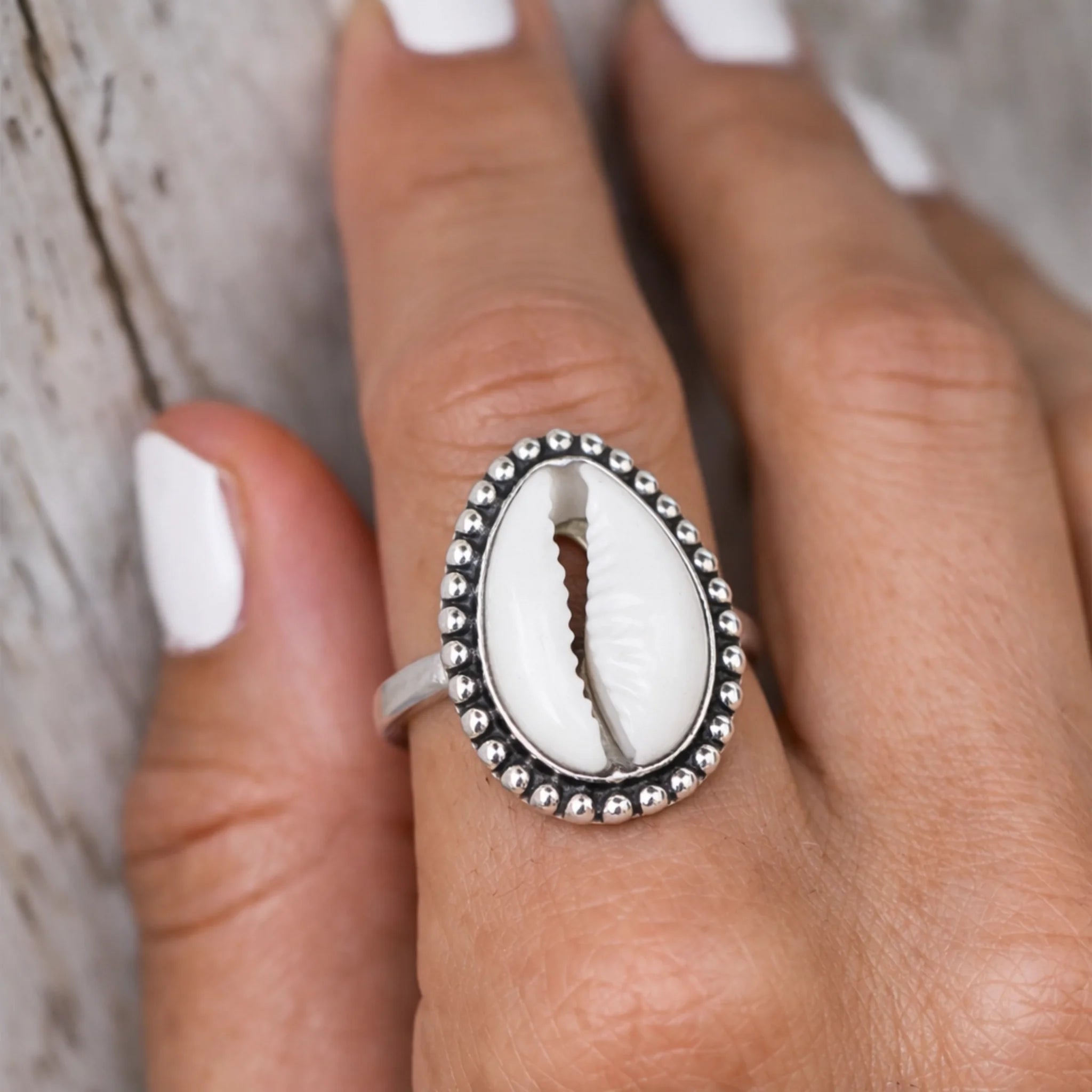 Silver ring with a central shell design on a finger against a neutral background