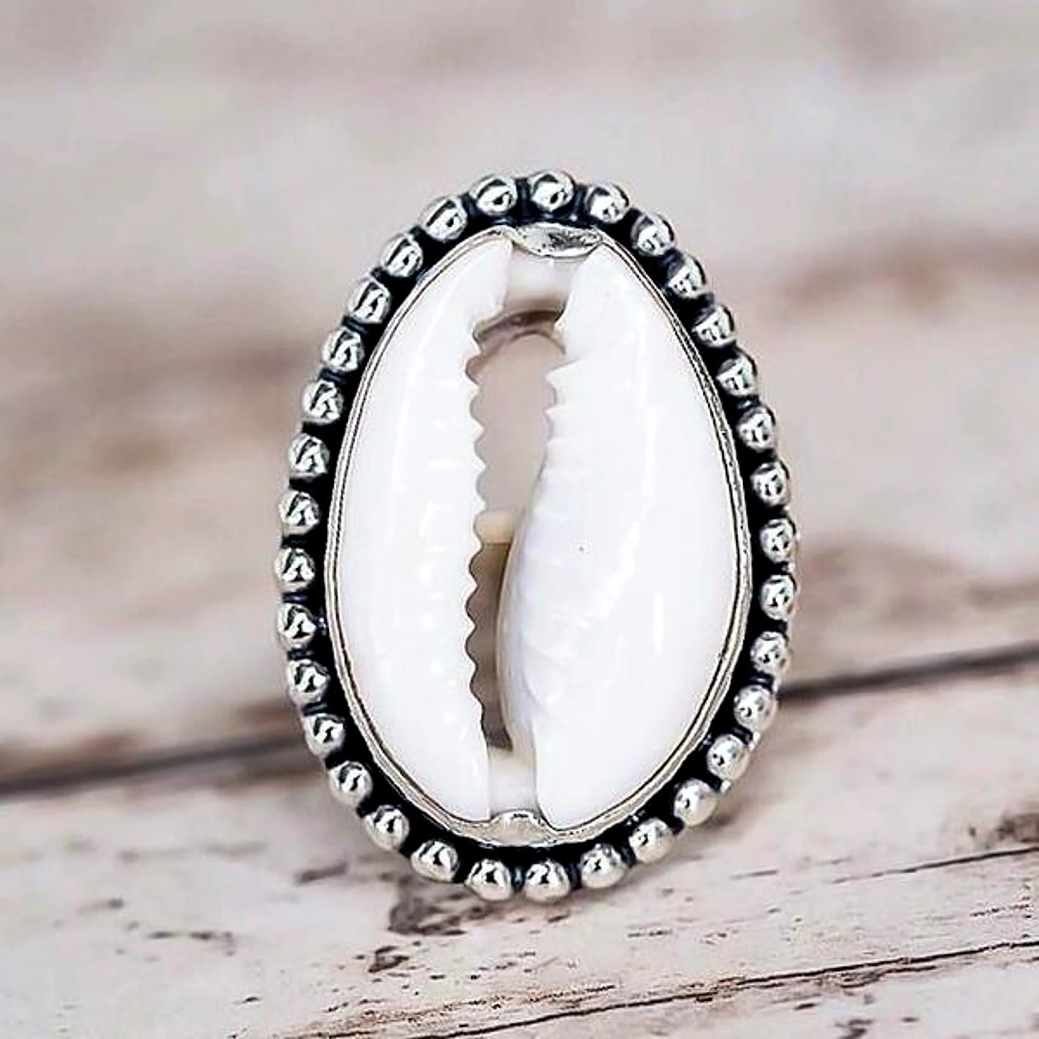 Silver ring with a white shell in the center on a wooden surface
