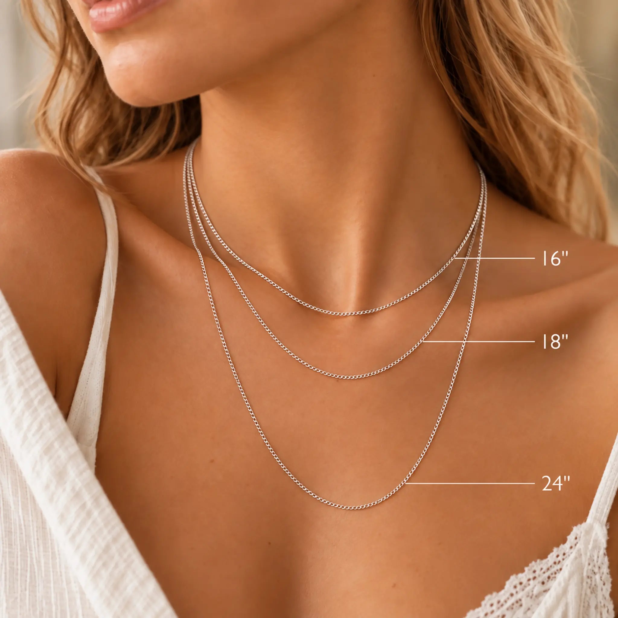 A close-up of a woman's neck and upper chest wearing three layered silver chain necklaces at different lengths, with size labels pointing to 16", 18", and 24".