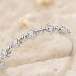 A close-up of a silver-toned diamond eternity ring resting on a textured beige surface.