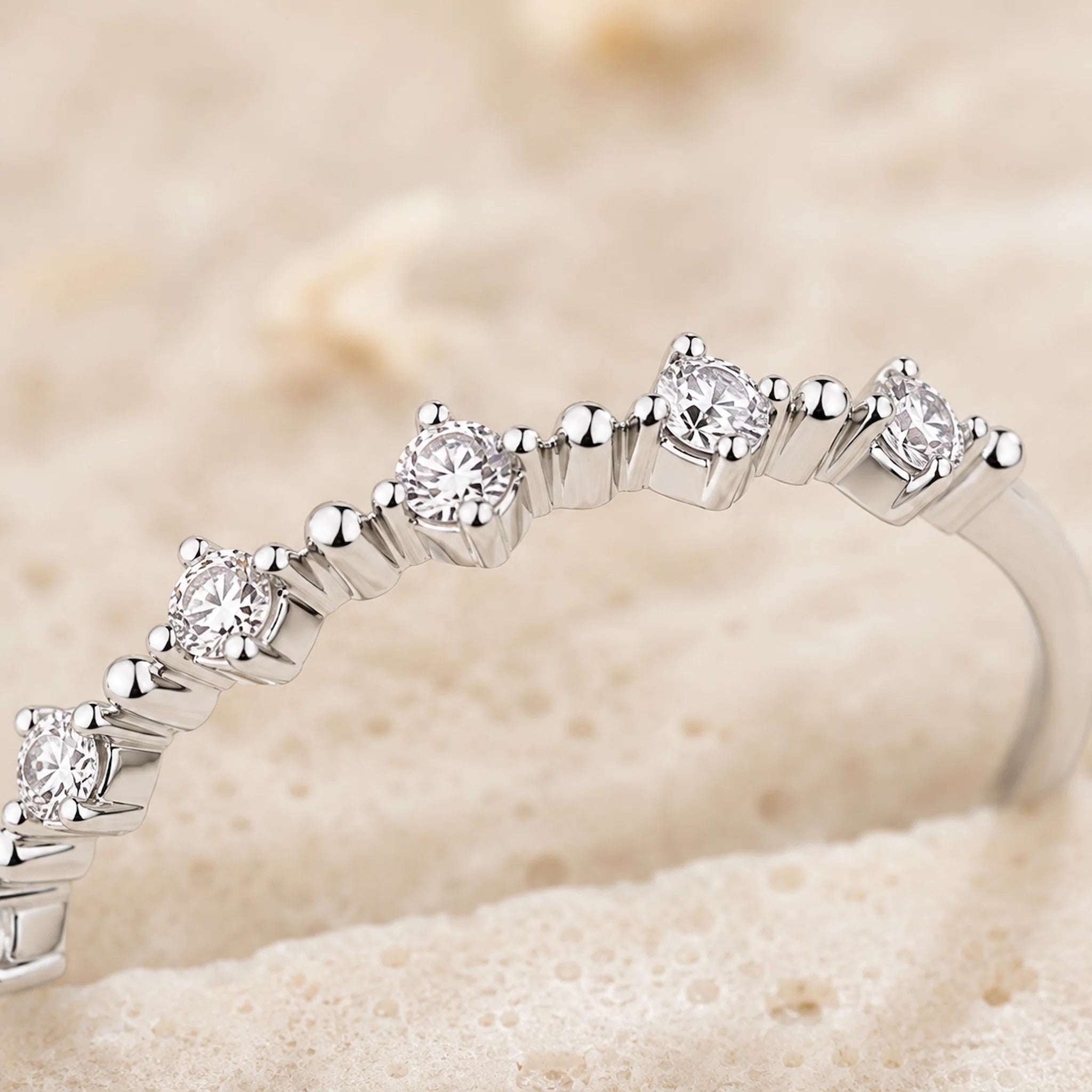 A close-up of a silver-toned diamond eternity ring resting on a textured beige surface.