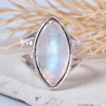 Silver ring with a marquise-shaped moonstone on a textured surface with dried grass. 