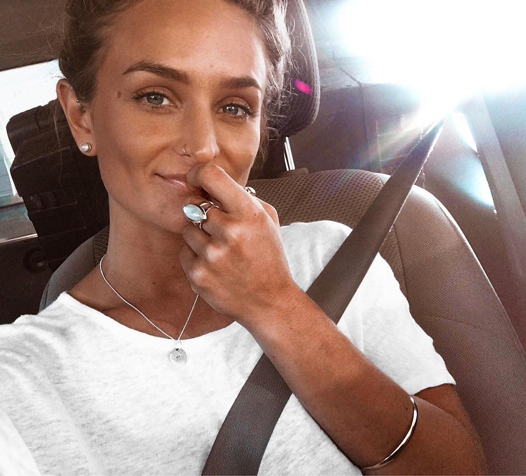 Woman sitting in a car with a seatbelt on, wearing a white top and indie and harper moonstone ring