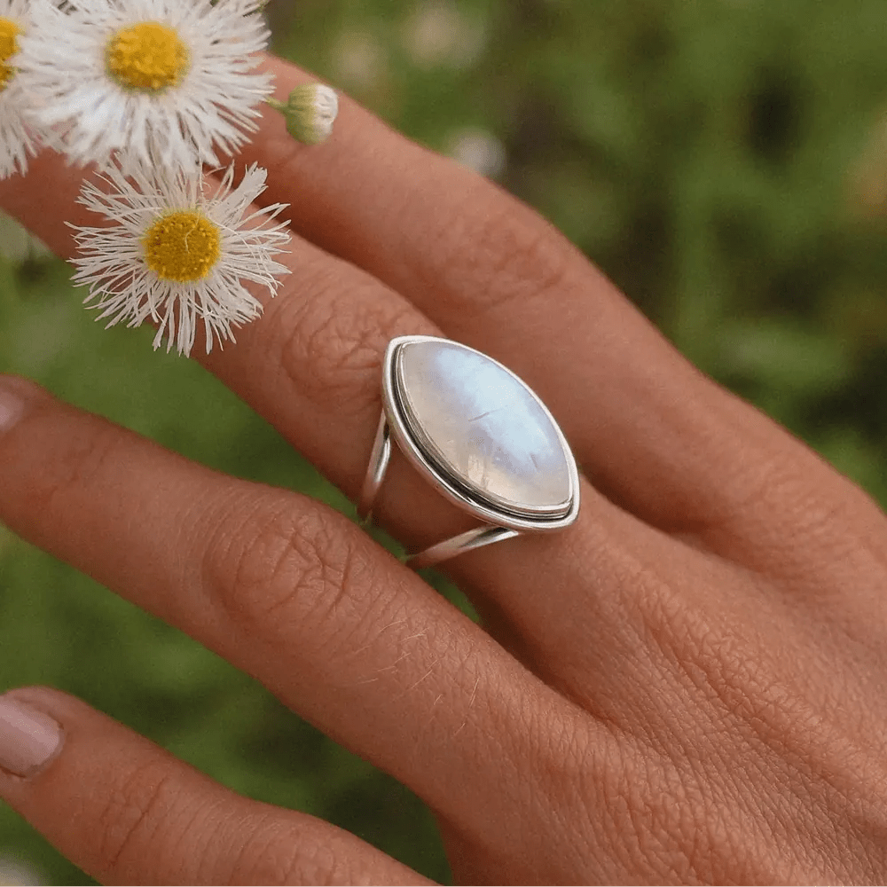 Hand wearing a silver ring with a rainbow moonstone on a blurred natural background 