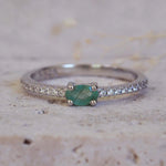 Silver emerald ring with a natural green emerald gemstone on a textured beige background