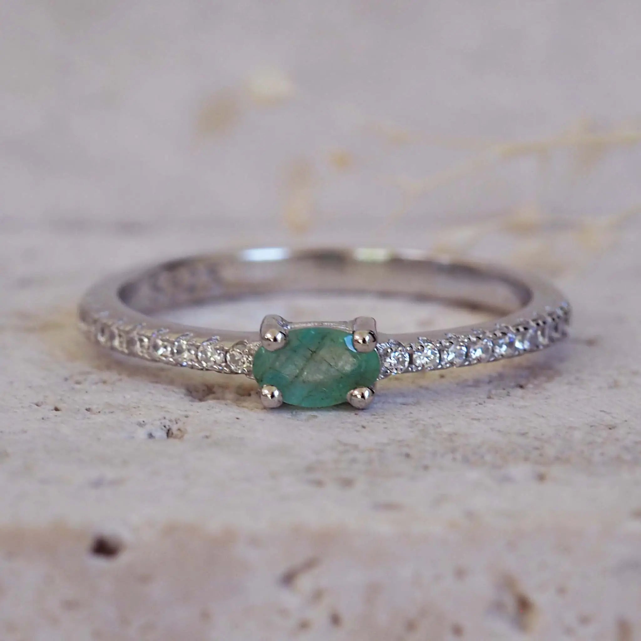 Silver emerald ring with a natural green emerald gemstone on a textured beige background