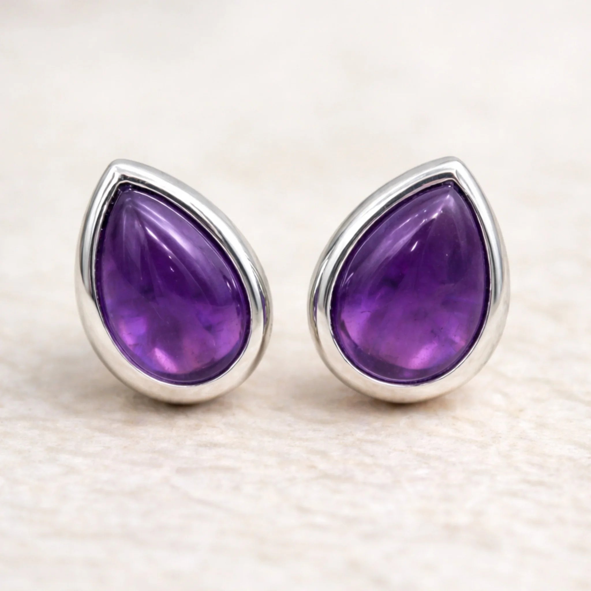 Pair of sterling silver stud earrings with february birthstone amethyst gemstones on a light background