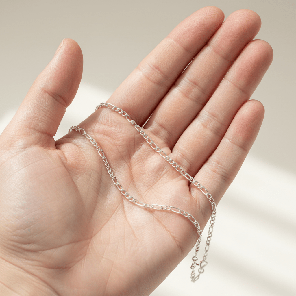Silver chain held in a hand against a neutral background