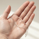 Silver chain held in a hand against a neutral background
