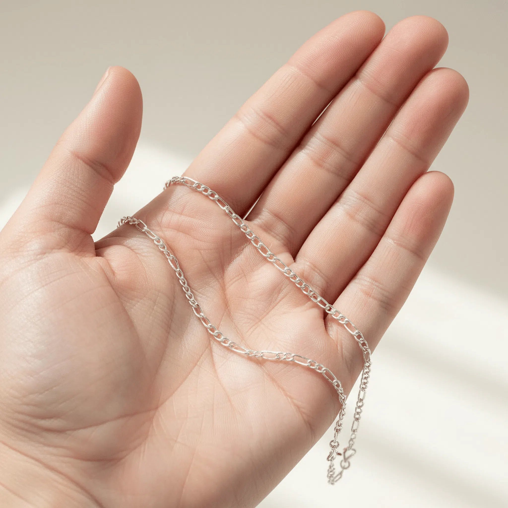 Silver chain held in a hand against a neutral background