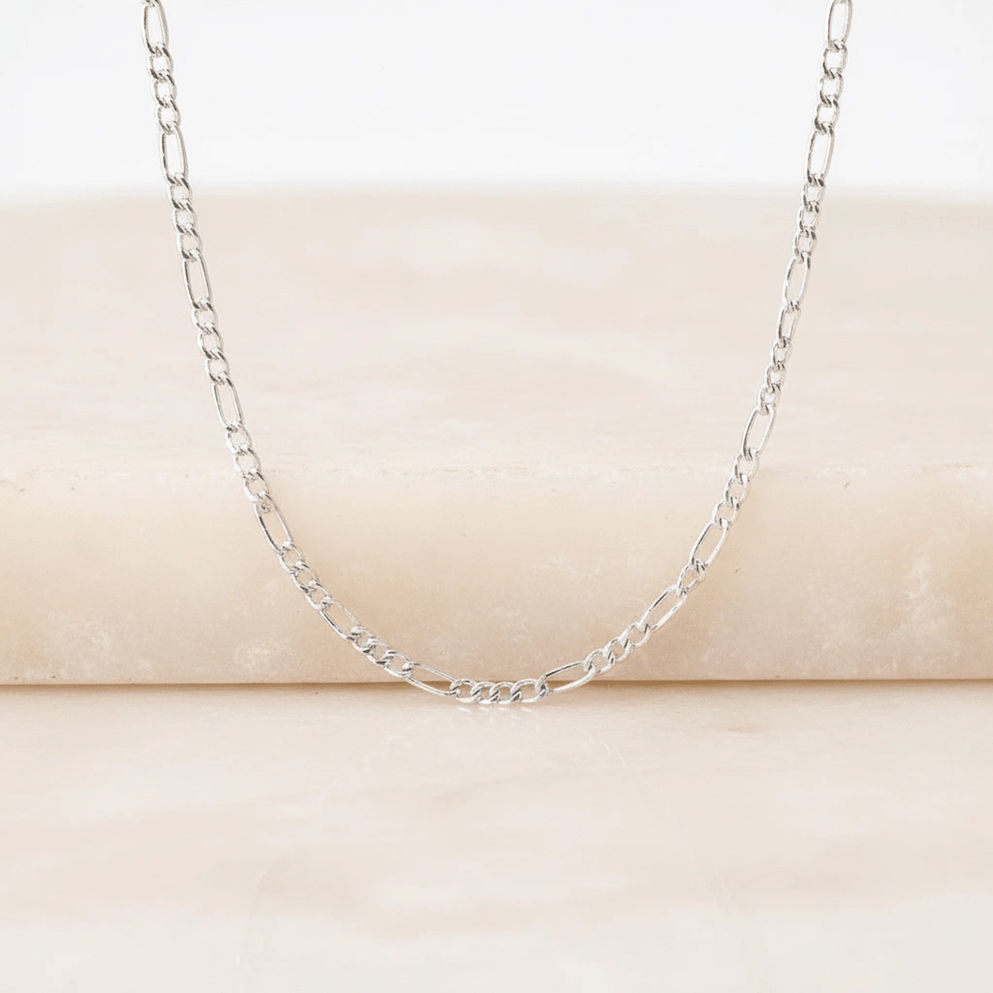 Silver chain necklace on a beige surface
