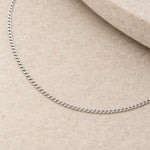 Close-up of polished 1.5 mm sterling silver flat curb links on pale stone