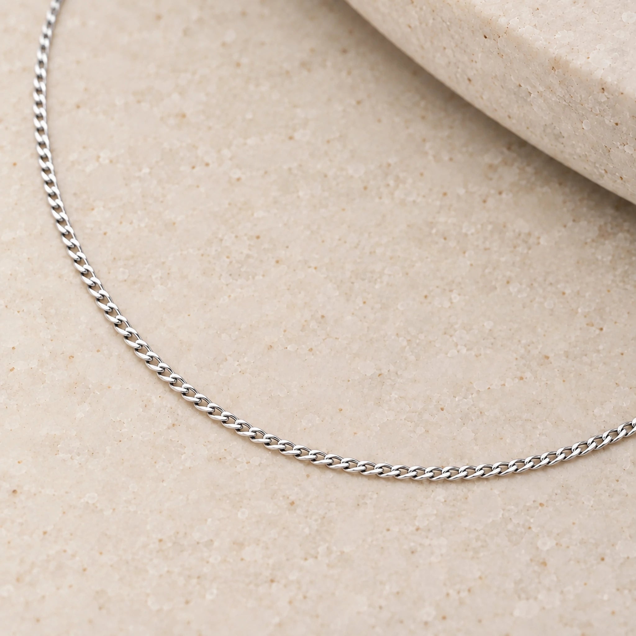 Close-up of polished 1.5 mm sterling silver flat curb links on pale stone