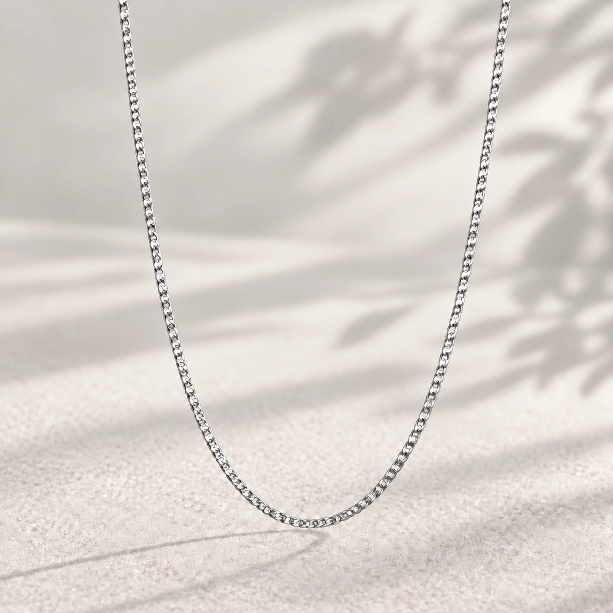 24 inch sterling silver flat curb chain, 1.5 mm, hanging against a soft neutral background