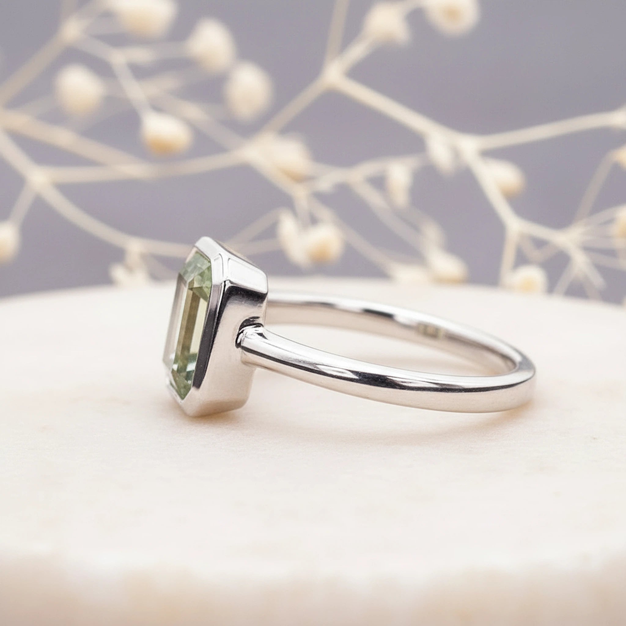 side view of a sterling Silver ring with a faceted natural green amethyst gemstone on a soft background