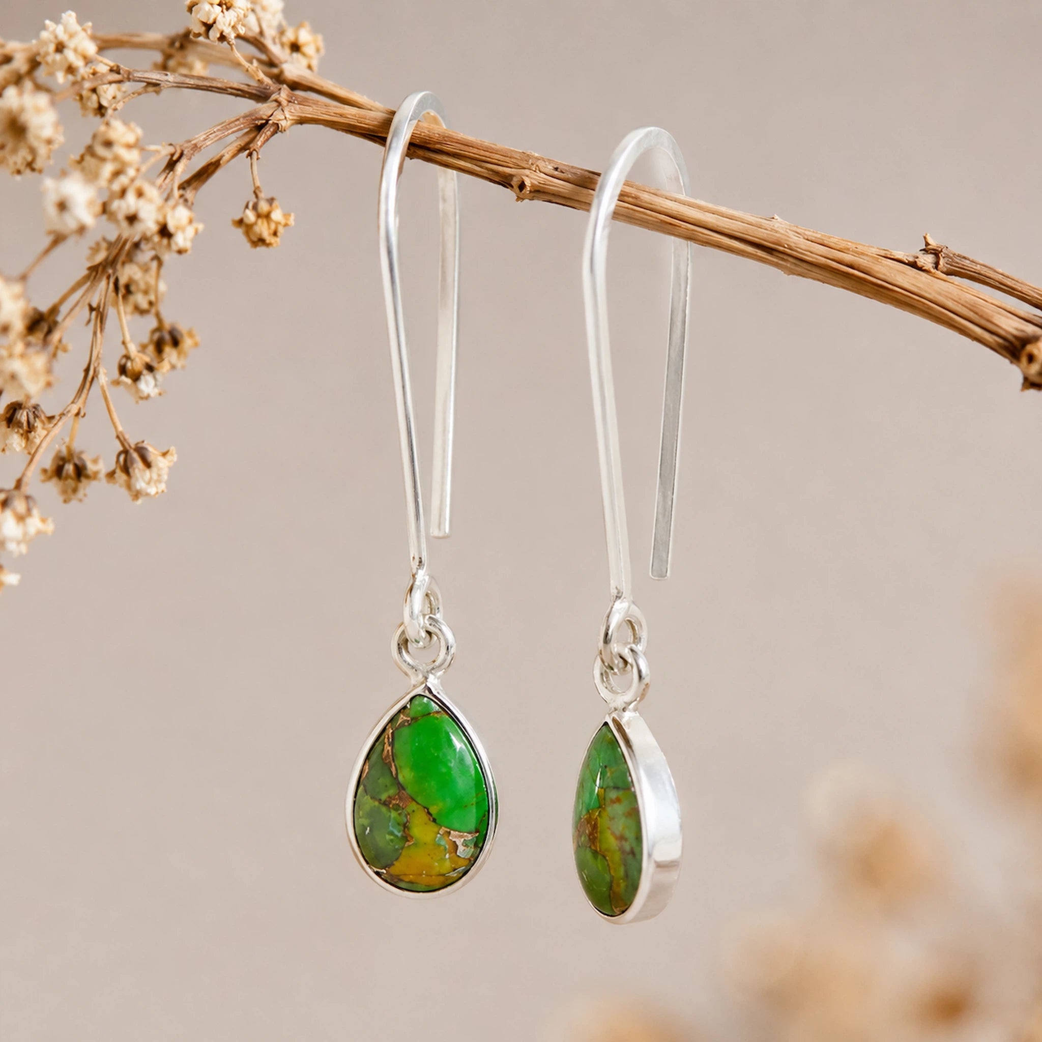 Silver hook earrings with green turquoise teardrop stones on a branch with dried flowers.