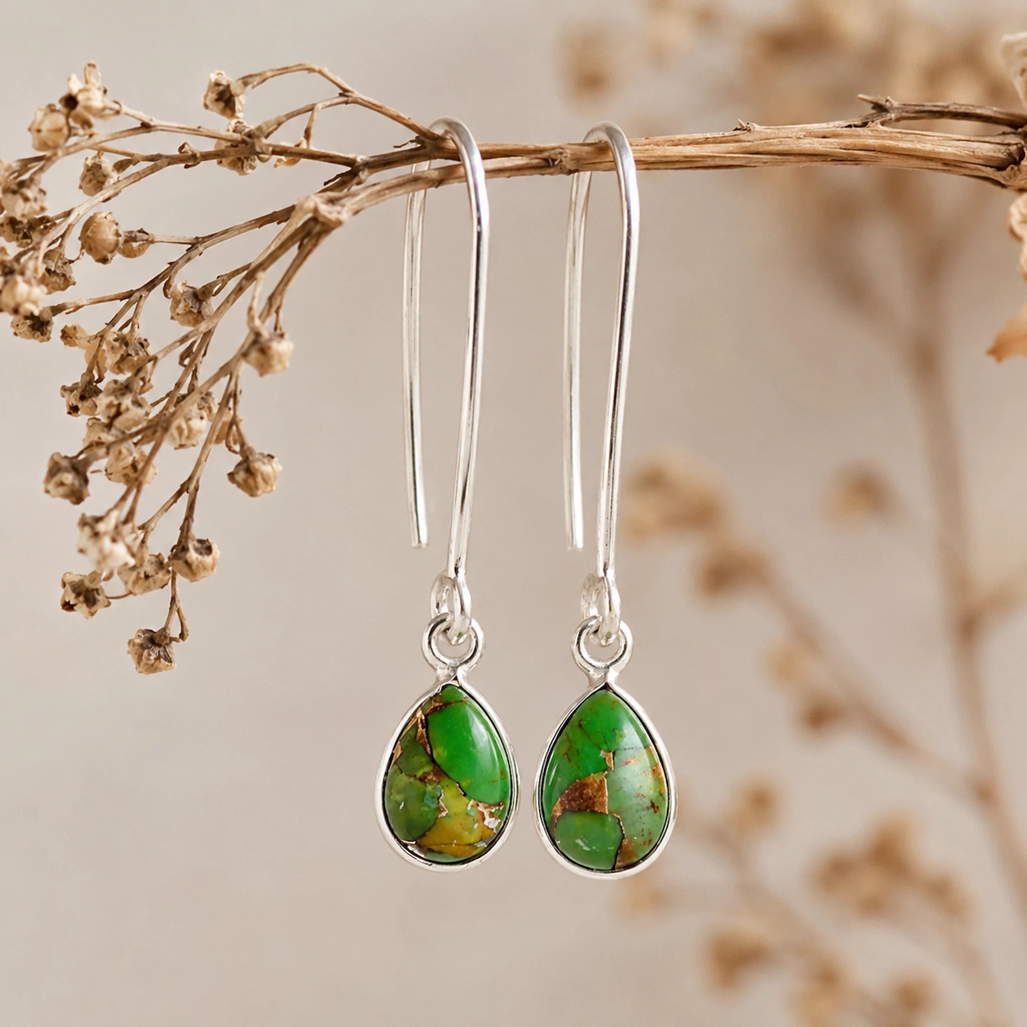 Sterling Silver elongated hook earrings with teardrop bezel set natural green turquoise gemstones hanging from a branch.