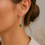 Close-up of a person wearing a green turquoise teardrop earring with a blurred background