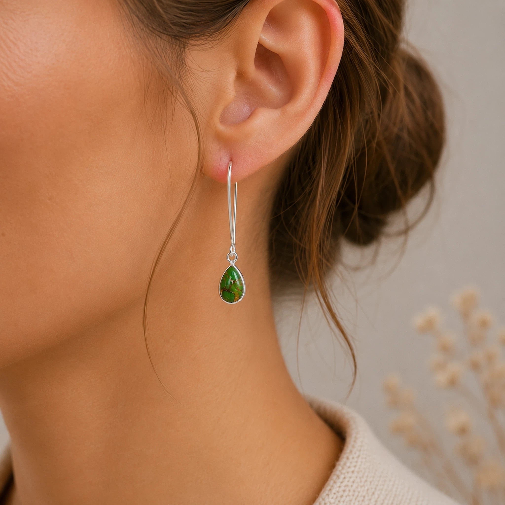 Close-up of a person wearing a green turquoise teardrop earring with a blurred background