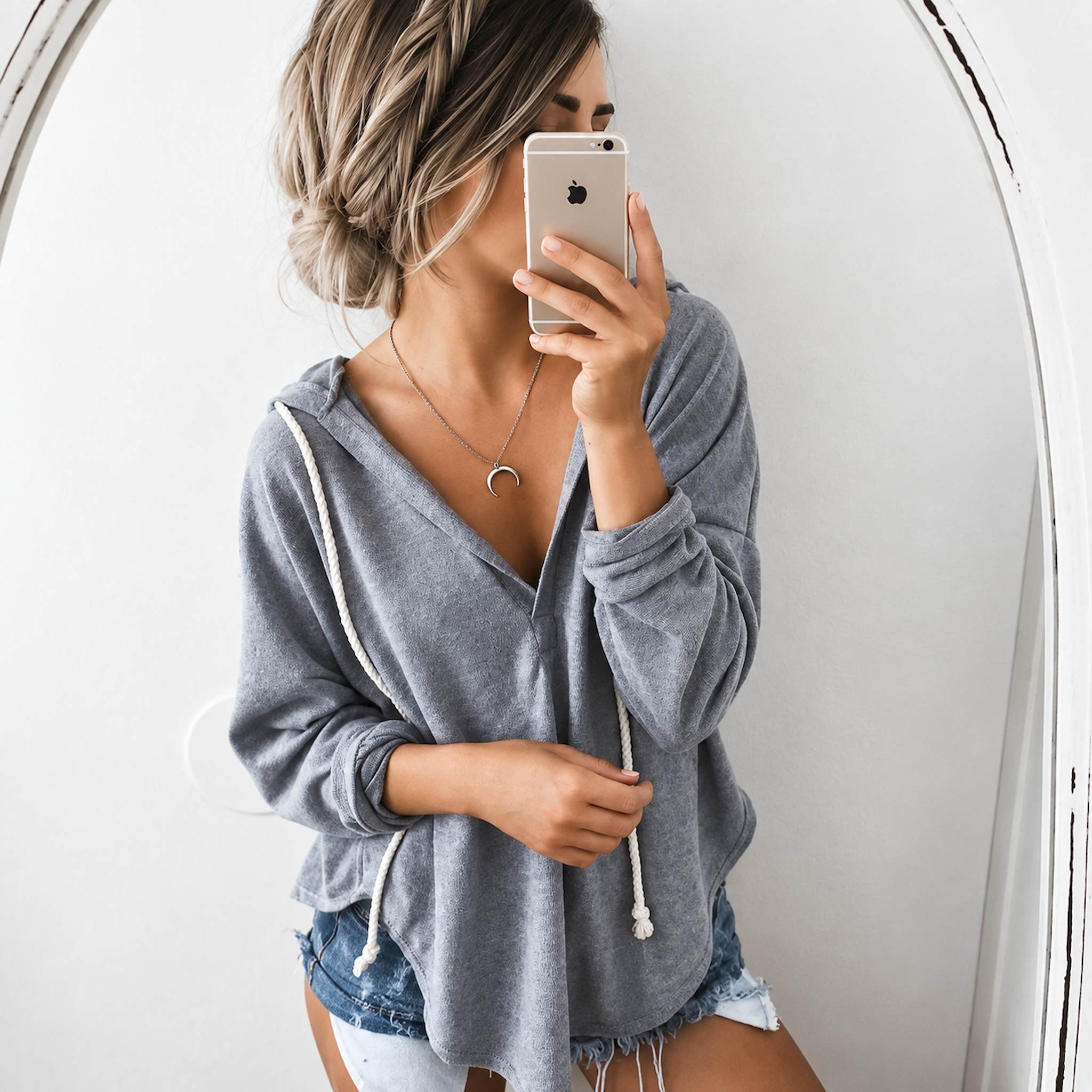 Person wearing a gray hoodie taking a mirror selfie, wearing a sterling silver necklace