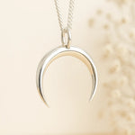 sterling Silver crescent moon pendant on a chain against a beige background