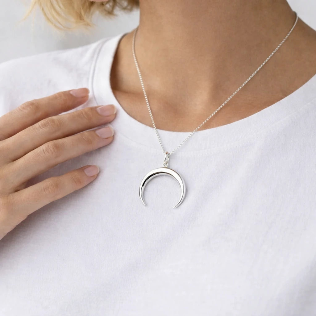 Silver necklace with a crescent moon pendant on a white shirt.
