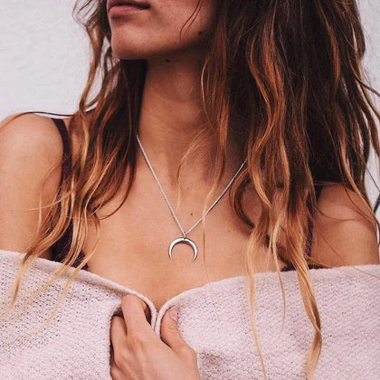 Woman wearing a silver necklace with a crescent moon pendant against a neutral background
