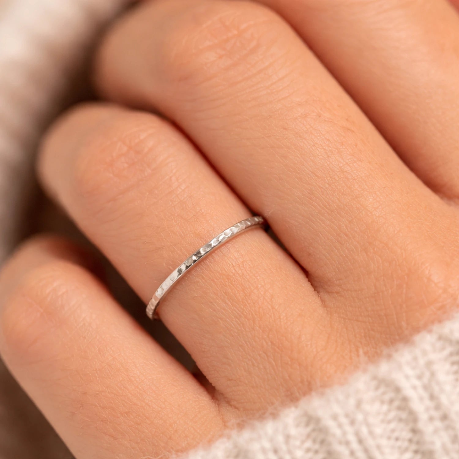 Close-up of a hand wearing a silver ring on a neutral background