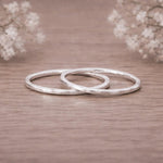 Two silver hammered stacker rings on a wooden surface with blurred flowers in the background