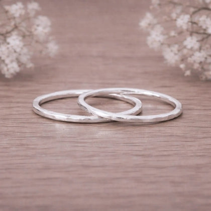 Two sterling silver hammered stacker rings on a wooden surface with flowers behind
