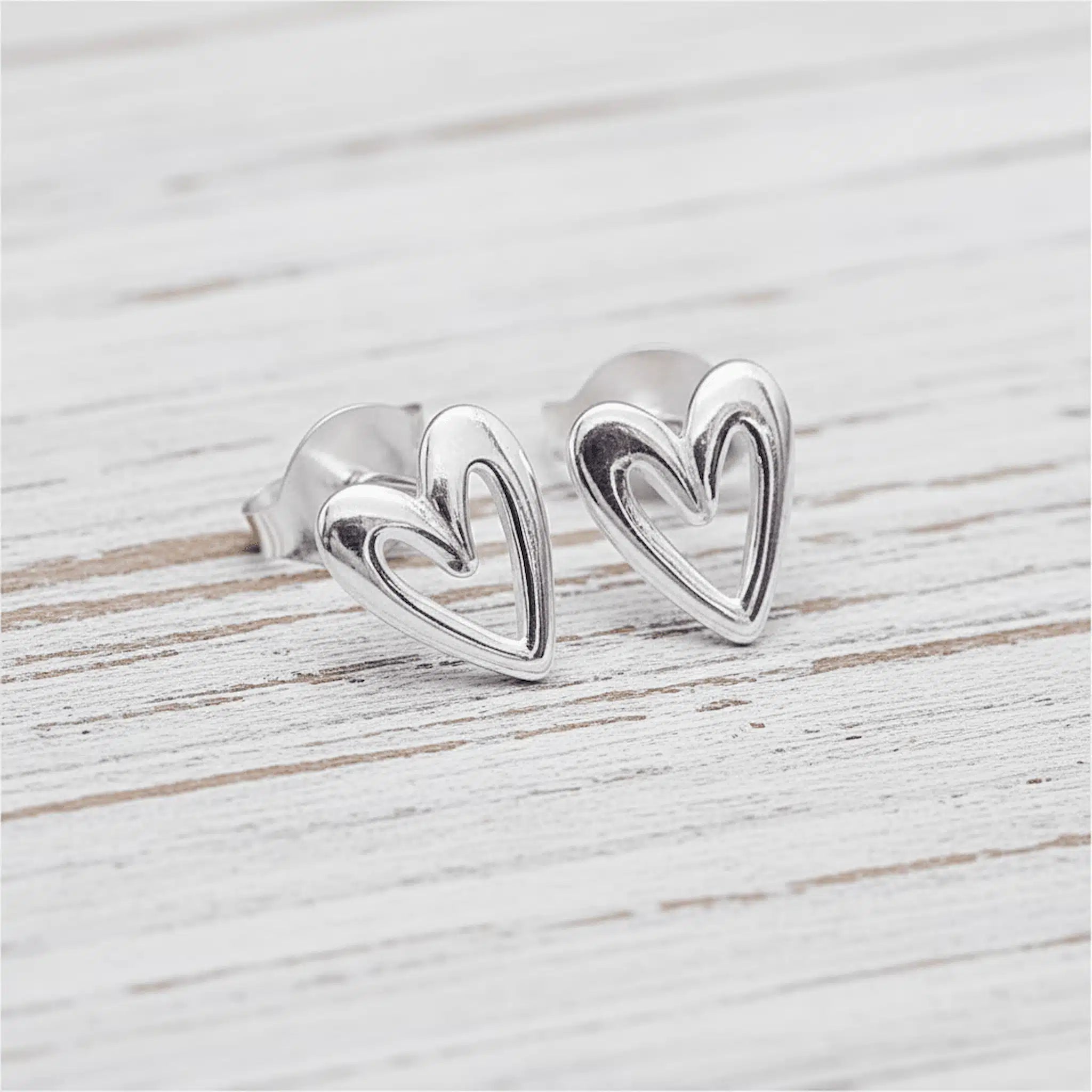 Silver heart-shaped earrings on a light wooden surface