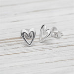 Silver heart-shaped stud earrings on a light wooden surface