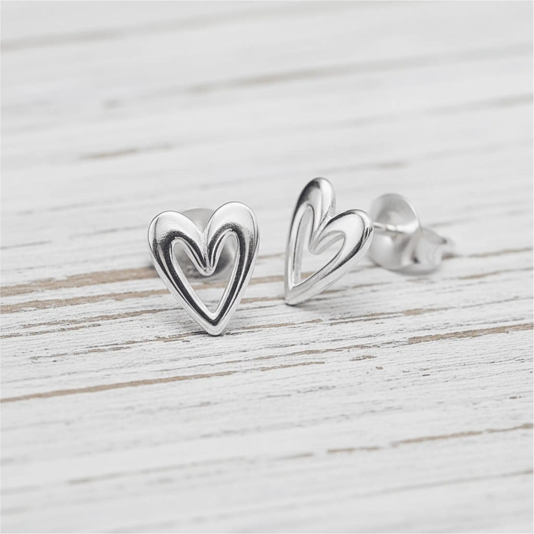 Silver heart-shaped stud earrings on a light wooden surface