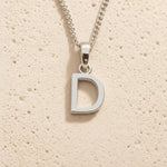 Silver necklace with a 'D' pendant on a beige textured background