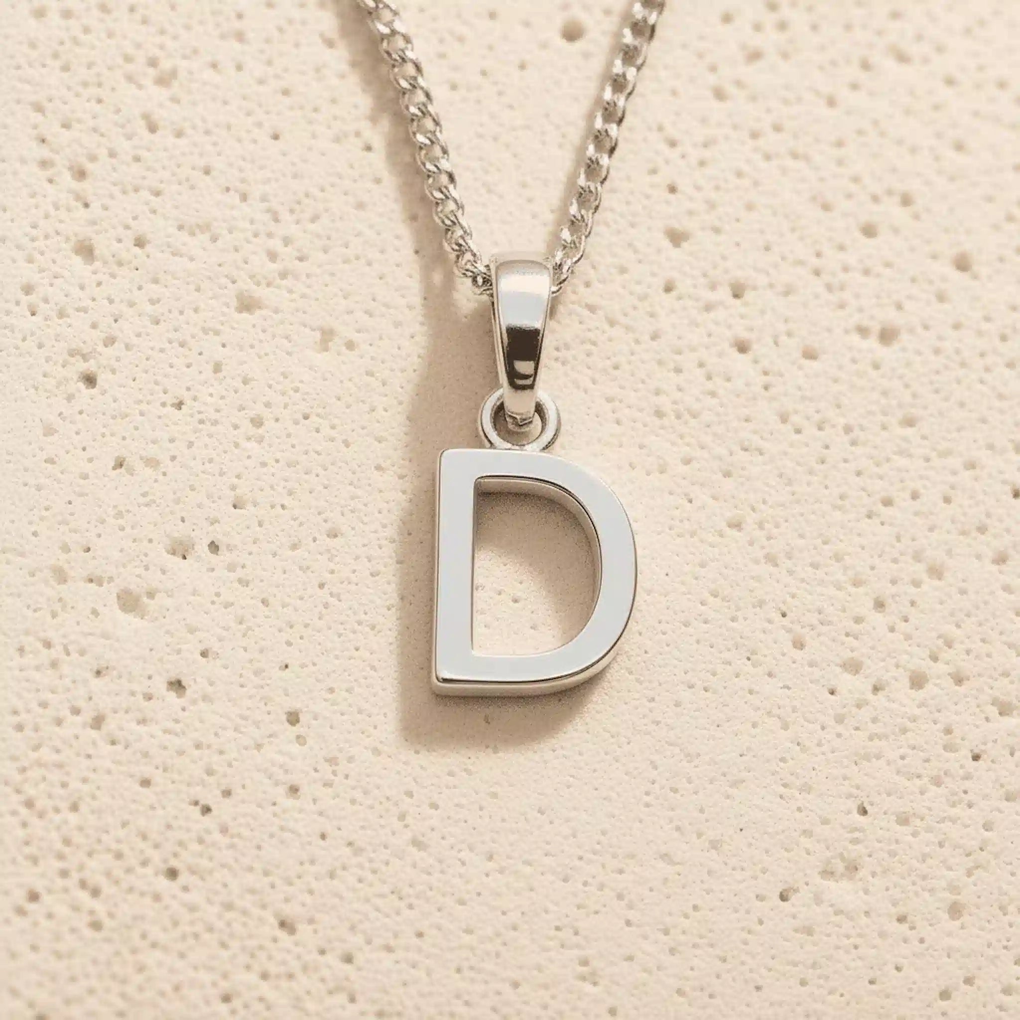 Silver necklace with a 'D' pendant on a beige textured background