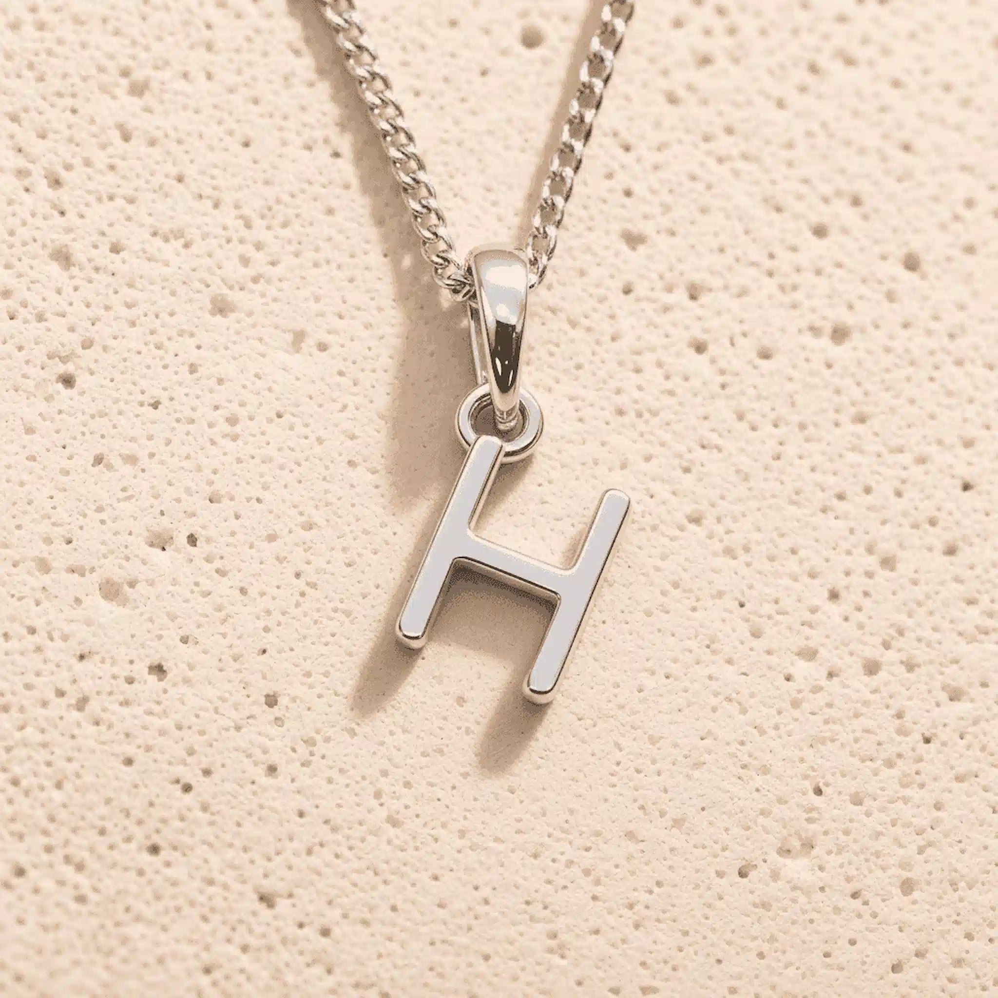 Sterling Silver Initial Necklace with a minimalist H charm pendant on a light stone background