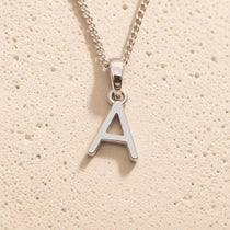 Sterling Silver Initial Necklace with a minimalist A charm pendant on a light stone background